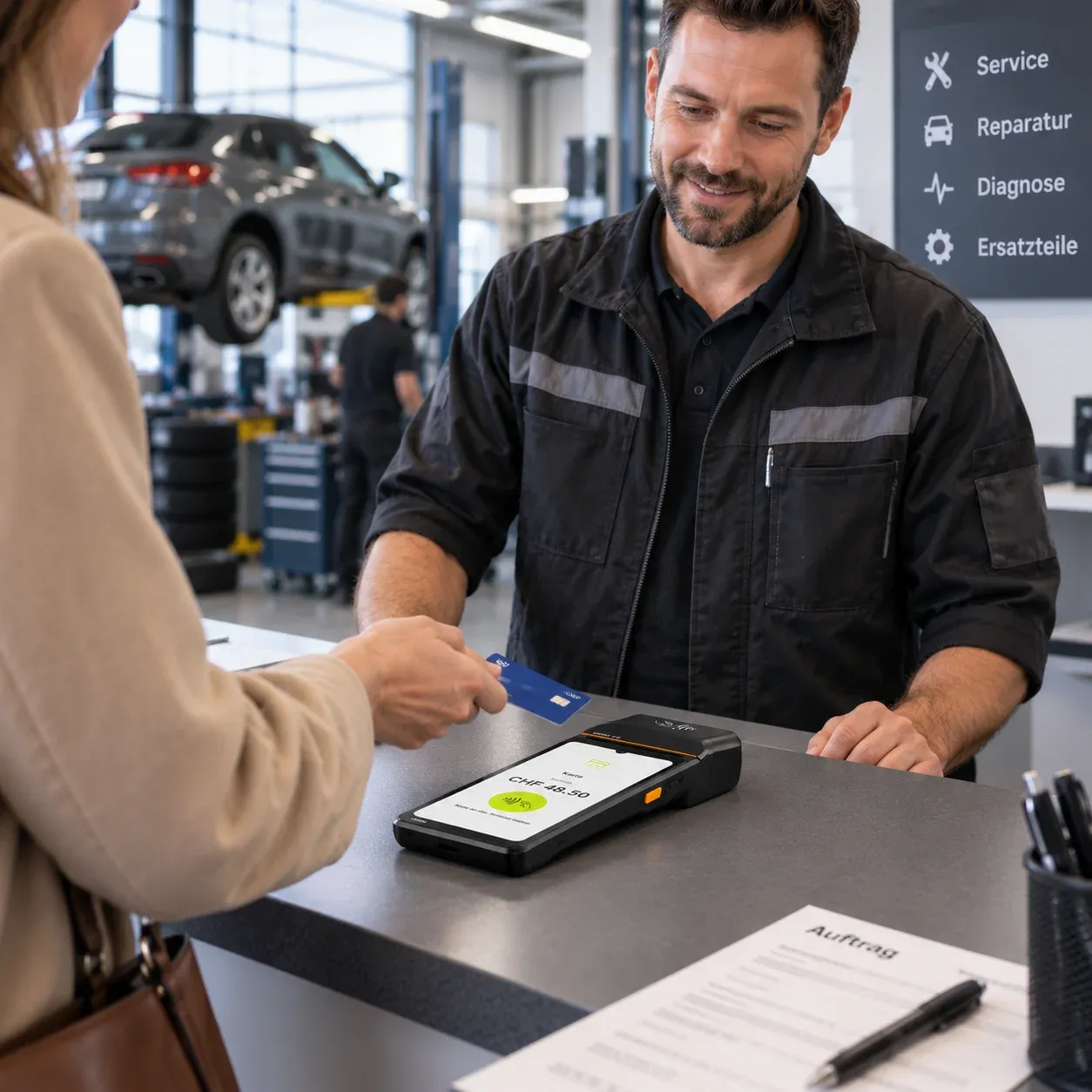 Eine Kundin bezahlt am Werkstattempfang kontaktlos mit der Karte am Terminal, daneben liegt der Auftrag; im Hintergrund ein Fahrzeug auf der Hebebühne